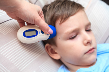 measuring the temperature with an infrared thermometer to a child, close-up. Coronavirus, flu. Home...