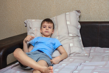 The child lies on the bed with a thermometer in his hands, measuring temperature. Virus, flu. Home quarantine