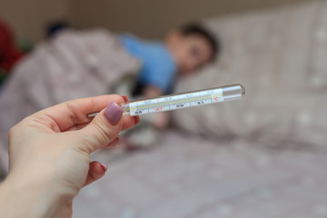 Mercury thermometer with temperature in hands close-up, on a blurred background with a child. Coronovirus. Disease