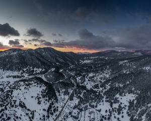 The Aerial view of a sunset over mountain in Arahova, Greece, a view of the valley below with trees covered by snow, colors of sunset