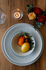 Easter table setting composition with traditional golden painted egg, beautiful tableware on natural dark wood textured table. Top view, copy space, close up, background.