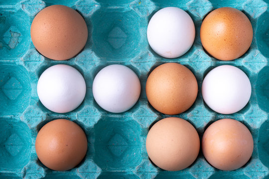 Code graphic top down image of white and brown shade chicken eggs in colourful teal egg carton box in studio lighting of food