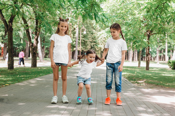 Three children in white t-shirts stand holding hands in park. Mock up.