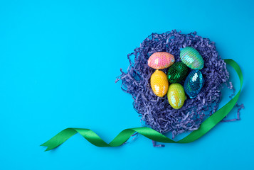 decorative Easter eggs from sequins lie in a nest of strips of paper on a blue background