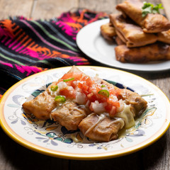 Mexican chimichanga with melted cheese and pico de gallo sauce on wooden background