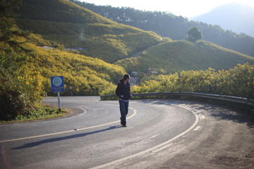 Fototapeta premium Man are strolling and Mountain scenery filled with yellow flowers or Mexican sunflower (Tung Bua Tong) at Doi Mae U Kho, Mae Hong Son, Thailand.