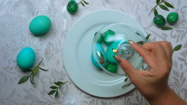 Easter preparations: female hands takes a glass dome off the white plate with green-colored easter eggs with foil bird image