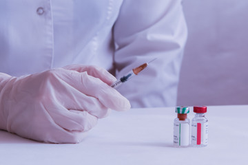 The coronavirus vaccine is ready for use. The doctor's gloved hand grabs the syringe. On the table in front of the doctor are vials of vaccine.