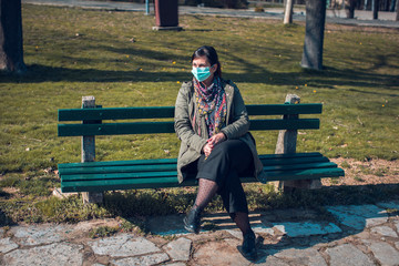 woman with protective face social distancing on empty park bench