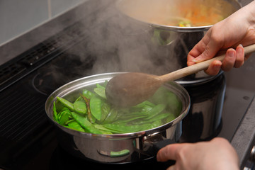 In the kitchen, colorful vegetables are cooked in a large nickel-plated pot.
