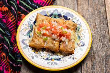 Mexican chimichanga with melted cheese and pico de gallo sauce on wooden background