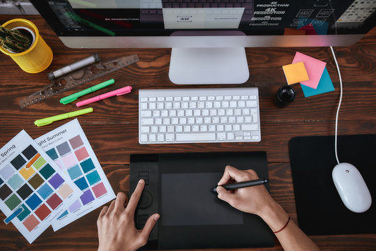 Right equipment. Top view of a designer using graphic tablet and working with computer while sitting at his workplace in the office. Top view of a workplace with graphic tablet, keyboard and computer.
