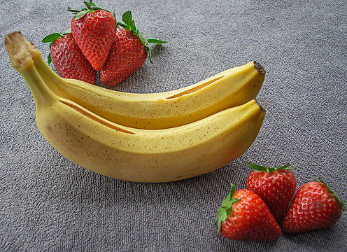 Fresas jugosas y pl&aacute;tanos,  sobre un fondo gris