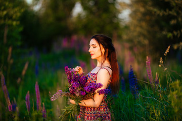 Naklejka premium beautiful girl in a lupine field. Girl holding a bouquet of lupines