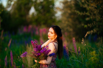 Pretty young woman in a field at sunset. holding flowers