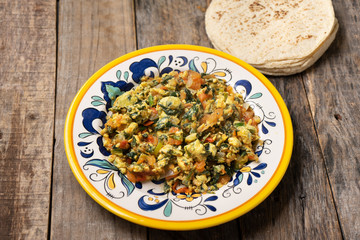 Mexican scrambled eggs with spinach on wooden background