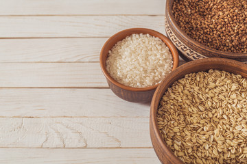 buckwheat, rice and oatmeal in brown clay plates on a white wooden background