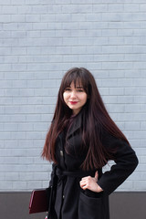 Student in black coat smiles against a brick grey wall