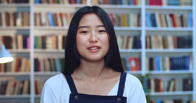 Portrait of nice beautifull asian student with black hair emotionally explaining and making a lot of gests by her hands in library.