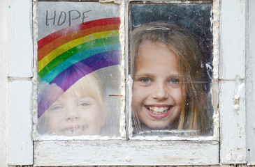 two young girls in grungy window with rainbow sign of hope