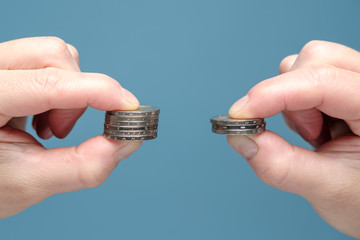 Hands are comparing two stacks of coins of different sizes, indicating a worsening financial...