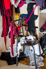 Sloppy things in the closet. Open wardrobe with clothes on hangers and clutter in open drawers