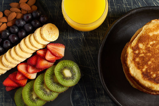Desayuno de frutas con panqueques y jugo de naranja sobre fondo oscuro