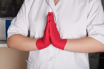 hands of a nurse in red rubber gloves folded for prayer