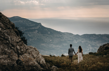 couple standing on the top of mountain, holding hands and watching sunset