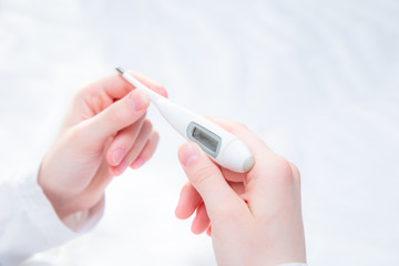 A young woman has the flu at home. In the woman's hands lies an electronic thermometer with a temperature reading after the measurement. Flu and colds, viral diseases.