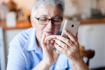 Senior woman using mobile phone at home. Retired person shopping online. People staying connected,...
