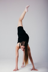 Beautiful gymnast in black sportswear standing on his hands on white background. Sporty girl doing a handstand