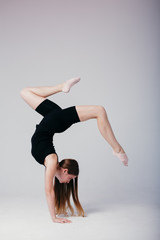 Beautiful gymnast in black sportswear standing on his hands on white background. Sporty girl doing a handstand.