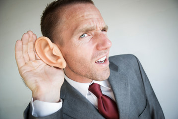 Funny businessman cupping his large ear straining to hear 