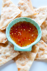 Close-up of fresh gourmet crispy flatbread wedges with bright red Thai sweet and sour chili sauce