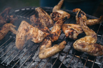 Grilling at summer weekend. Fresh meat preparing on grill. Lifting chicken wings with pair of tongs. Assorted delicious grilled meat.