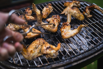 Grilling at summer weekend. Fresh meat preparing on grill. Lifting chicken wings with pair of tongs. Assorted delicious grilled meat.