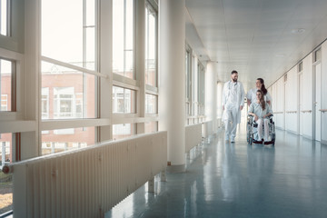 Doctor, nurse, and patient in wheelchair on hospital corridor
