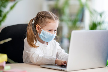 little girl in mask, with Teddy bear, doing homework, e-learning