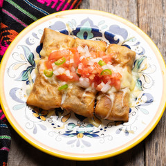 Mexican chimichanga with melted cheese and pico de gallo sauce on wooden background