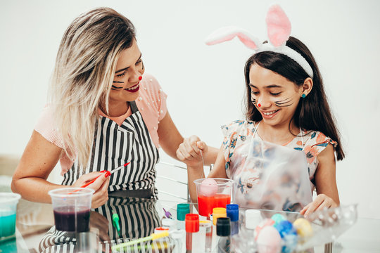 A mother and her daughter painting Easter eggs. Happy family preparing for Easter. Cute little girl wearing bunny ears on Easter day. Happy easter!