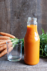 Carrot juice in a glass bottle and an empty glass nearby. In the background a bunch of fresh carrots with green tops. Wood background. Vertical orientation