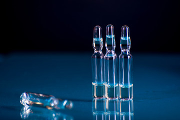 Glass ampoules with liquid for injection against laboratory flasks on dark background.