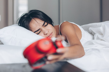 Wake up of young sleepy angry woman stopping alarm clock on the bed