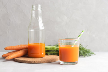 A glass bottle with fresh carrot juice on a cork stand and a glass with juice and a cocktail straw nearby. In the background a bunch of fresh carrots. Place for text.