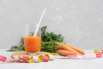 A glass with fresh carrot juice and a cocktail straw. A centimeter, a measuring tape in the foreground and a bunch of carrots in the background. Diet. Healthy eating