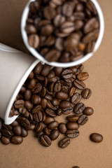 Two gray paper cups filled with coffee beans. One cup is upset. Close-up, flat lay.