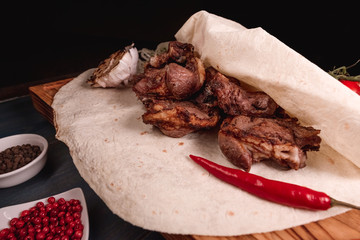 Appetizing fried meat lies on a wooden tray, among the seasonings. Studio photography of food in the cooking industry, dark background