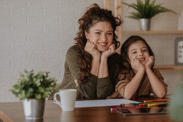 Happy family. Mother and daughter are posing in front of camera while drawing at home.