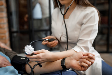 Cropped image. Female doctor measuring blood pressure to older patient sitting at sofa